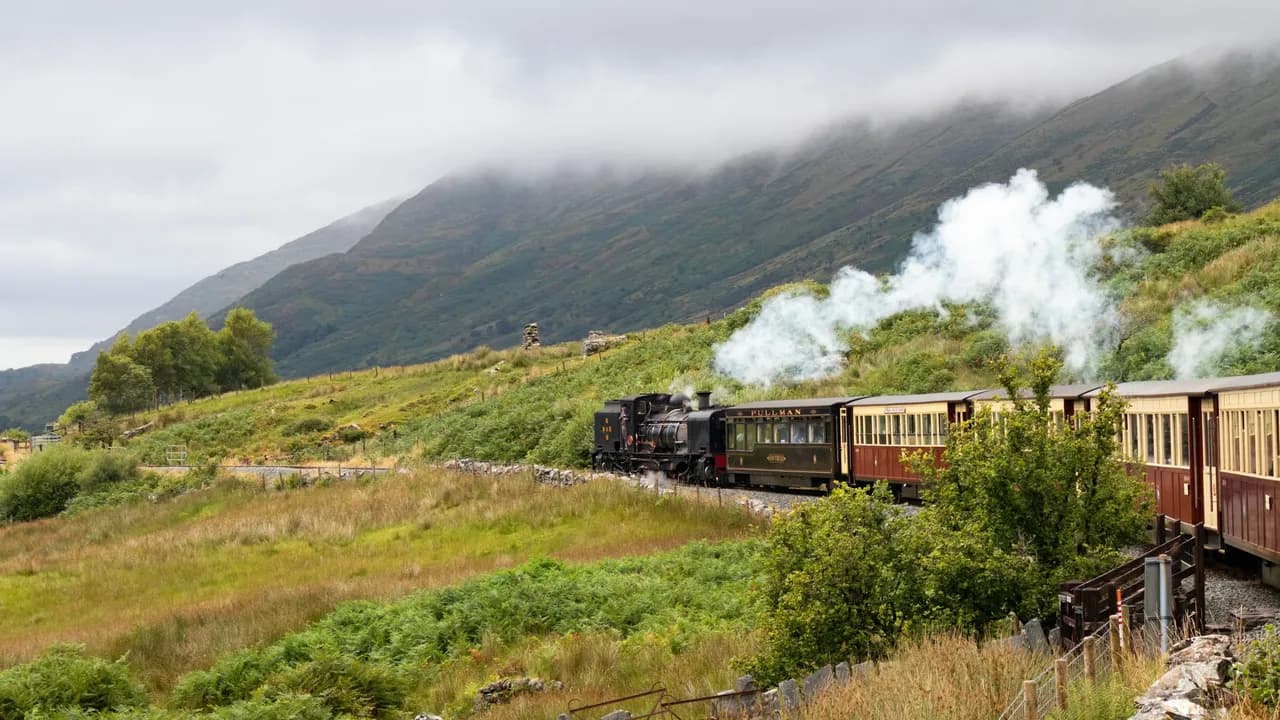 A Garratt steam engine hauling a train beneath misty Snowdonia hills on the Welsh Highland Railway